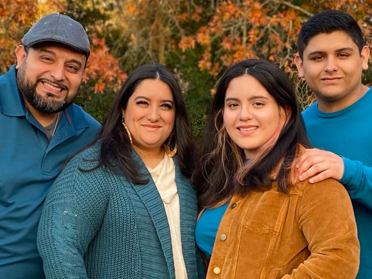 Family photo of a hispanic family dressed in fall colors of teal and brown in front of trees with fall leaves